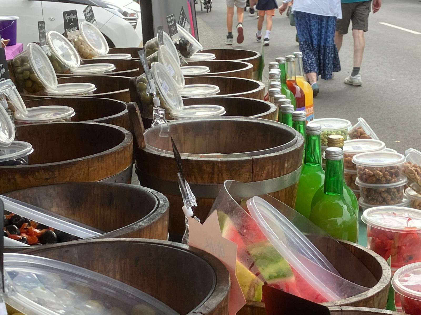 Wide view of market stall with apple juice bottles and olive displays