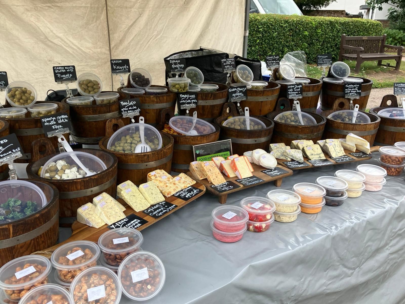 Full market stall display with olives in wooden buckets, cheeses and dips