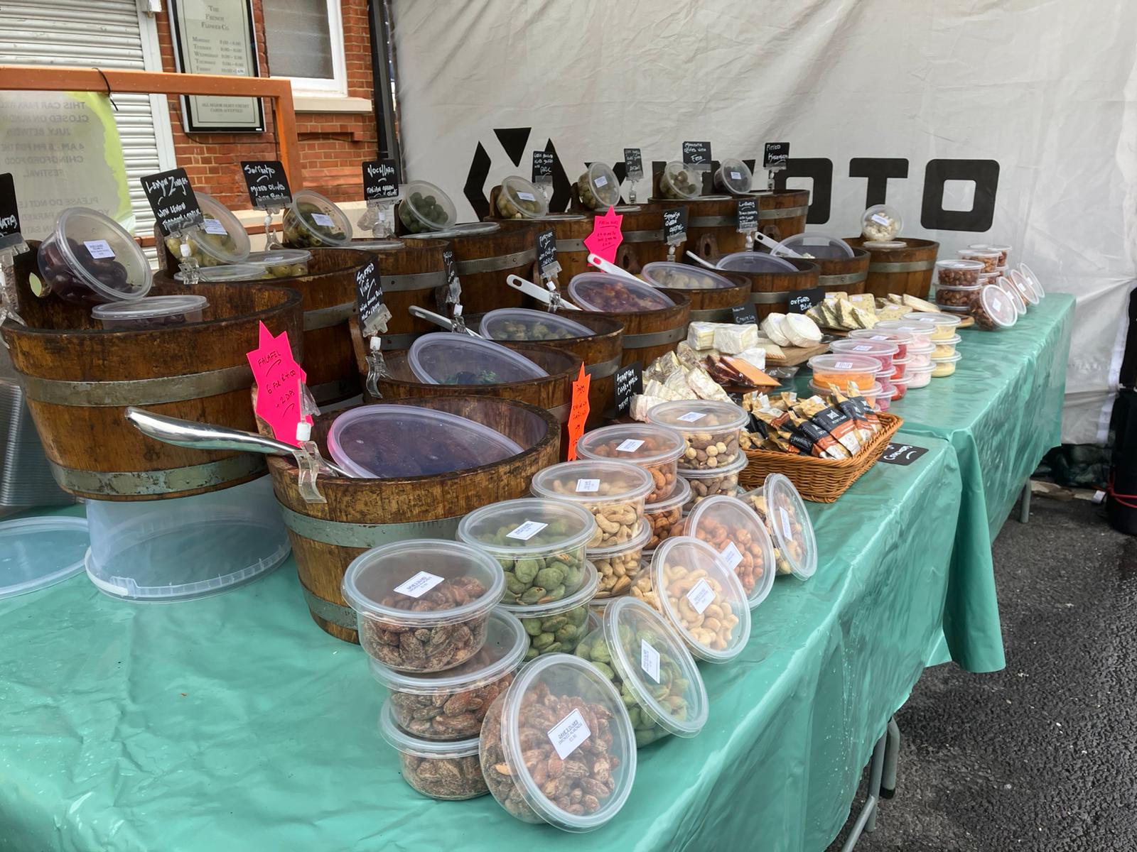 Market stall with wooden barrels of olives and customers browsing
